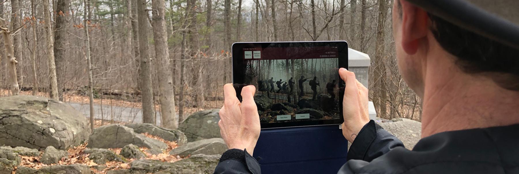 Person standing outside holding up a tablet with a scene from the Gettysburg AR Experience app