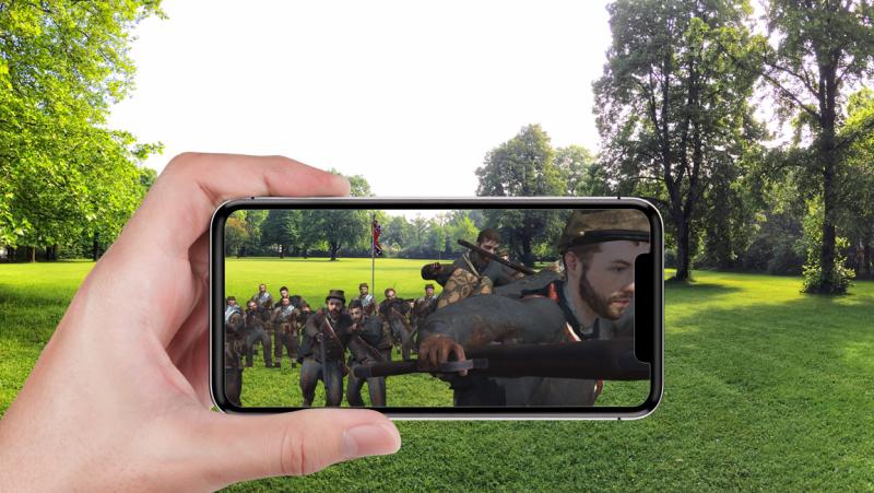 A hand holds a mobile phone horizontally with an AR scene shown on the screen while outside