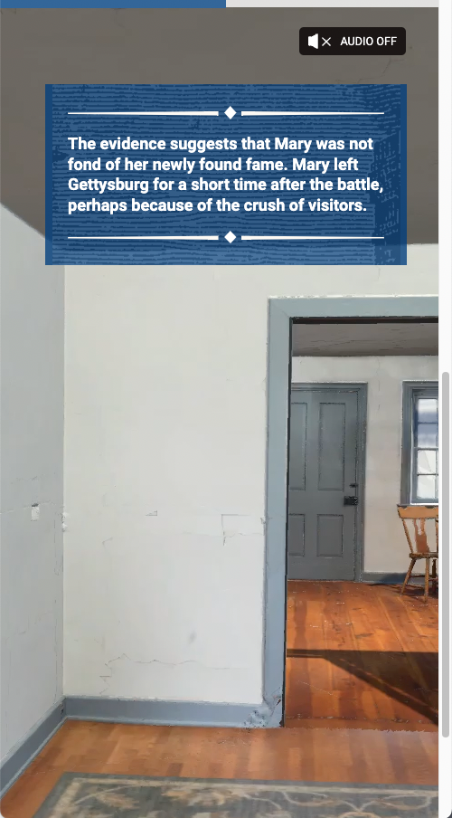 Screenshot. Shows a room in Mary's stone house. White walls with blue trim and wood floors. Text on screen reads: The evidence suggests that Mary was not fond of her newly found fame. Mary left Gettysburg for a short time after the battle, perhaps because of the crush of visitors.