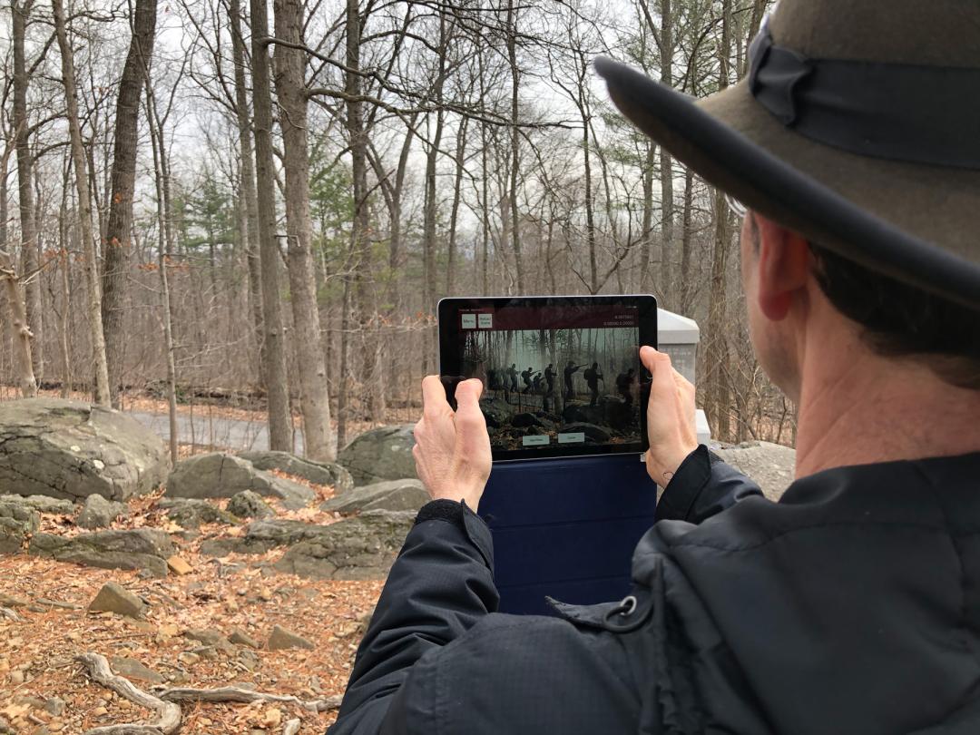 Person standing outside holding up a tablet with a scene from the Gettysburg AR Experience app